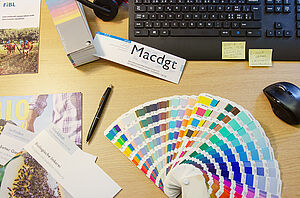 Bürotisch mit Farbfächer, Merkblätter, Magazin, Tastatur und Computer