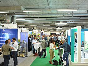 On the left and on the right there are stands of different companies, in the middle participants walk on a green carpet.