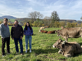 Drei Personen auf einer Wiese mit Kühen.