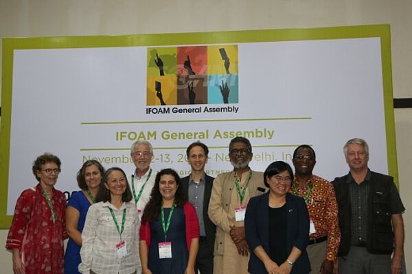 10 Menschen stehen vor dem IFOAM General Assembly Poster.