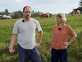 Un homme et une femme avec des vaches en arrière-plan.