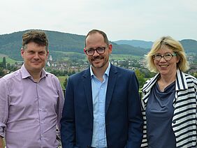 The three members of the Board of Directors on the roof of the FiBL restaurant smile at the camera, with Frick in the background