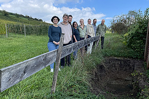 Eight people are standing next to a soil profile.