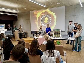 Acht Schüler*innen der Kantonsschule Zug präsentieren ihre Ergebnisse vor einem Publikum