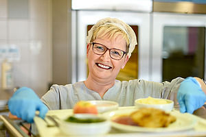 Frau in Kantine gibt Essen aus. 