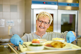 Frau in Kantine gibt Essen aus.