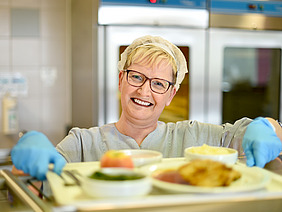 Frau in Kantine gibt Essen aus. 