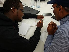 Two men sitting on a table and discussing some papers.