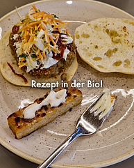 Ein beiger Teller hat ein sehr leckeres Burger-Menu darauf: Ein helles Brötchen mit einem Patty und Salat darauf, dazu Tempeh mit Mayo.