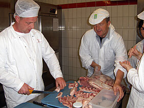 Mehrere Personen zerlegen Fleisch in Stücke.