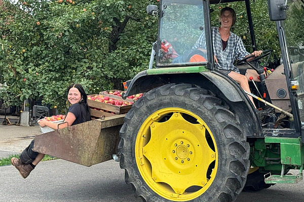 Frau sitzt am Steuer eines Traktors und transportiert Äpfel und eine junge Frau.