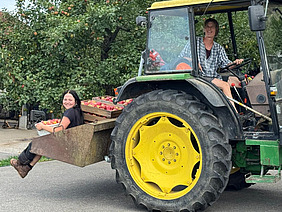 Frau sitzt am Steuer eines Traktors und transportiert Äpfel und eine junge Frau.