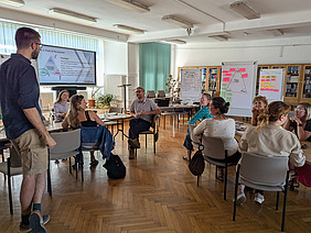 Workshopteilnehmende sitzen an Tischen in einem Raum.