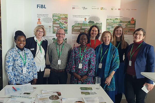 Acht Menschen an einem Stand lächeln für ein Foto.