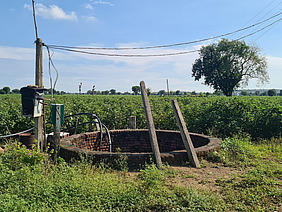 Ein alter Brunnen in einer grünen Landschaft.