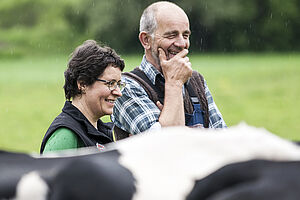 Two people standing next to each other laughing, in the foreground the back of a cow is visible