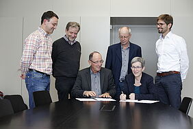 Members of FiBL, HAFL and SFS are gathered around a table, two people are sitting at the table and signing a contract.