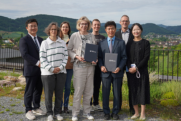 Eine Gruppe von Leuten mit Dorf und Bergen im Hintergrund.