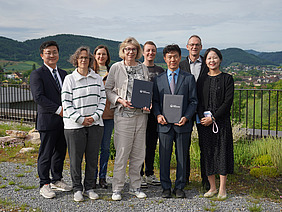 Eine Gruppe von Leuten mit Dorf und Bergen im Hintergrund.