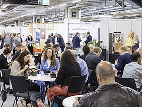 Exhibitors at their stands and sitting at tables.