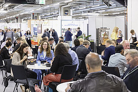 Exhibitors at their stands and sitting at tables.