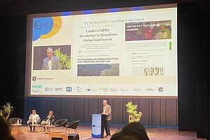 A speaker at the podium in front of a presentation