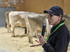 Eine Frau am Mikrofon, im Hintergrund Kühe