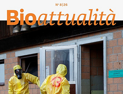 Copertina di Bioattualità 8|26: Tre persone in tute protettive e maschere respiratorie all’ingresso di una stalla.
