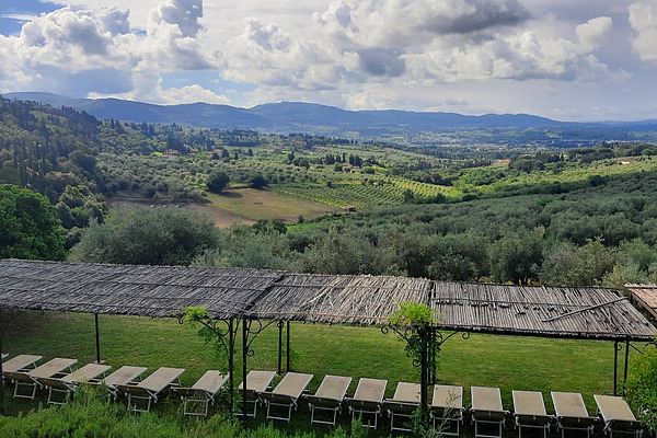 In the foreground are covered sun loungers; in the background is a rolling Tuscan landscape dotted with olive trees. 