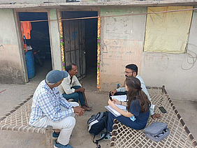 Vier Personen sitzen vor einem Haus und diskutieren.