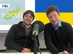 Tobias Eisenring und Toralf Richter hinter dem Mikrofon, dahinter das FiBL Podcast Logo und die Ukraine Flagge