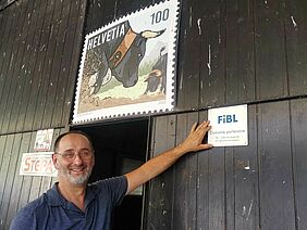 Homme devant la porte d'une grange, pointant une plaquette du FiBL.