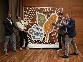 Vier Personen, die auf ein grosses OWC-Logo zeigen.