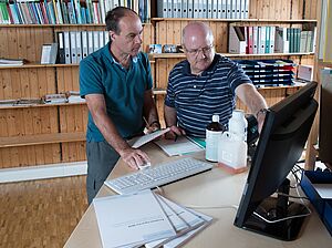 Employees of the group discuss something in front of a computer.