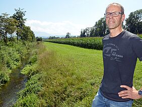 Ein Mann steht auf einem Feld, durch das ein Bächchen fliesst.