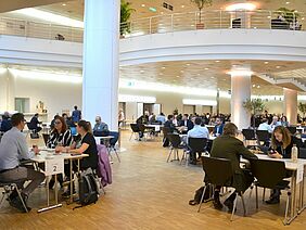 A bright room full of tables with 3-5 people in business dresses