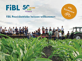 Banner der FiBL Karawane, mehrere Leute sitzen auf Traktoranhängern und blicken auf ein Feld