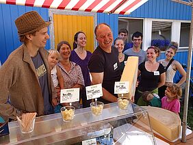 Alfred Schädeli with a piece of fresh cheese surrounded by people.