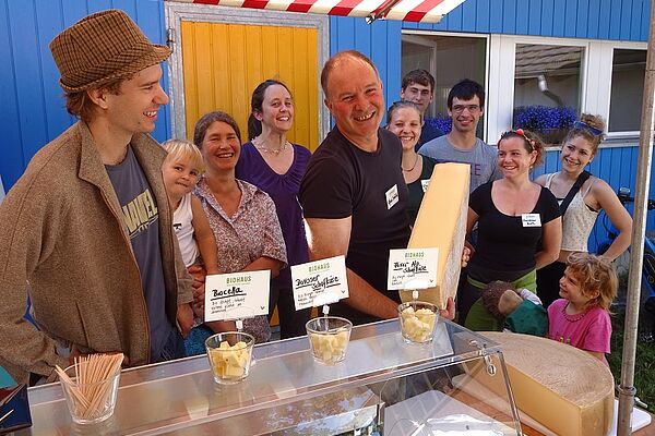 Alfred Schädeli with a piece of fresh cheese surrounded by people.