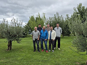 Photo de groupe de six hommes debout dans une oliveraie.