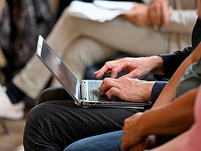 Eine Person hat einen Laptop auf dem Schoß und tippt auf die Tastatur.