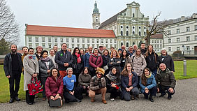 A group photo of around 35 smiling people in front of a historic building.