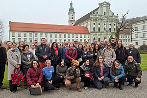 A group photo of around 35 smiling people in front of a historic building.