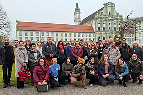 Gruppenfoto mit rund 35 lachenden Personen vor einem historischen Gebäude.