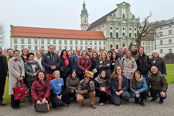 Gruppenfoto mit rund 35 lachenden Personen vor einem historischen Gebäude.