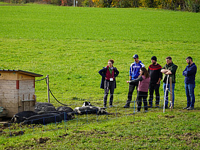 Eine Gruppe Schweine und eine Gruppe Menschen auf einer Wiese.