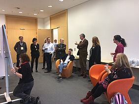 Group of people, some standing, some seated, one person writing on a flip chart.