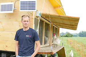 A man in front of a mobile chicken coop.