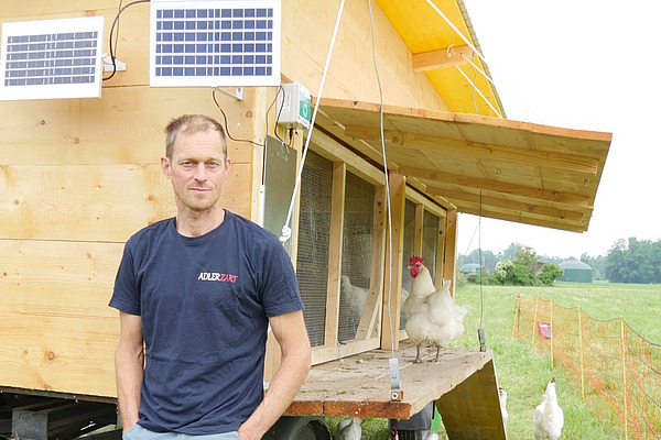 Ein Mann vor einem mobilen Hühnerstall.