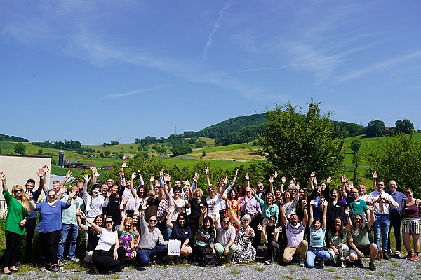 Eine Gruppe von etwa 50 Personen auf einem sonnigen Dach mit grünen Hügeln im Hintergrund.